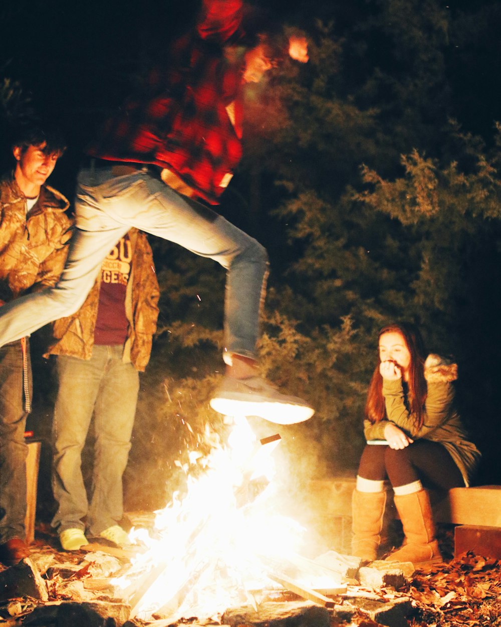 man wearing red and black checked shirt jumping near bonfire