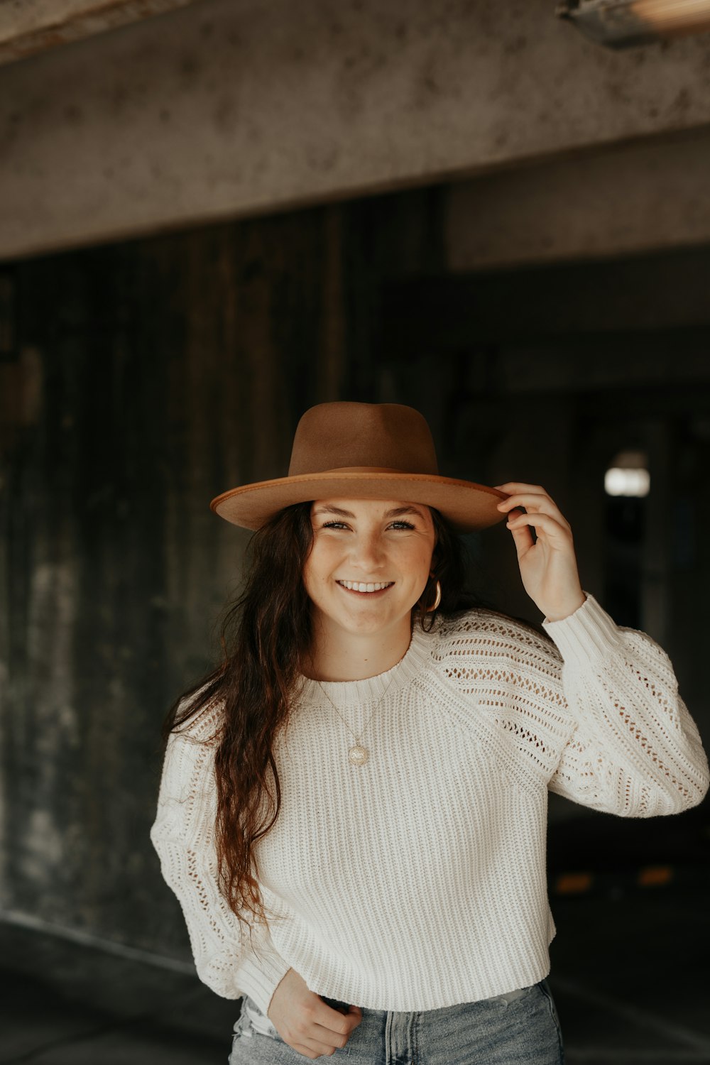 woman smiling and looking at the camera while holding brown hat