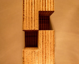 A structure composed of stacked rectangular wooden blocks with visible grain patterns. The design creates an architectural aesthetic, casting shadows on the background.