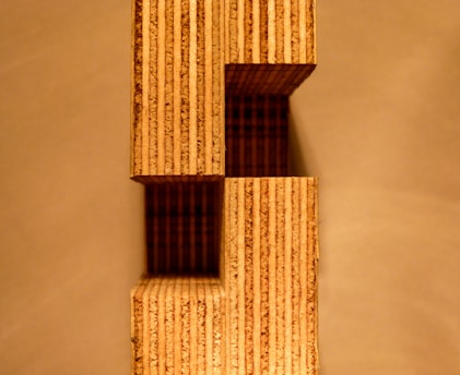 A structure composed of stacked rectangular wooden blocks with visible grain patterns. The design creates an architectural aesthetic, casting shadows on the background.