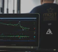 Dark-themed modern office workspace with a laptop and financial charts on screen.