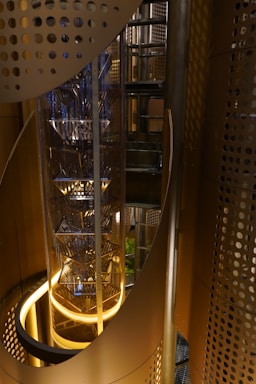 A modern elevator shaft with glass walls illuminated by soft blue lighting, showcasing sleek machinery.