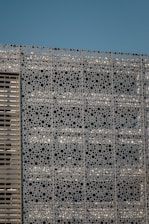 Close-up of a perforated metal panel installed on a modern building facade under sunlight.