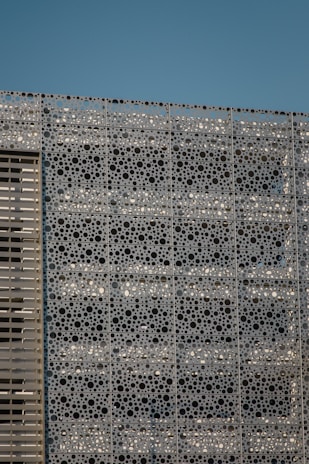 Close-up of a perforated metal panel installed on a modern building facade under sunlight.