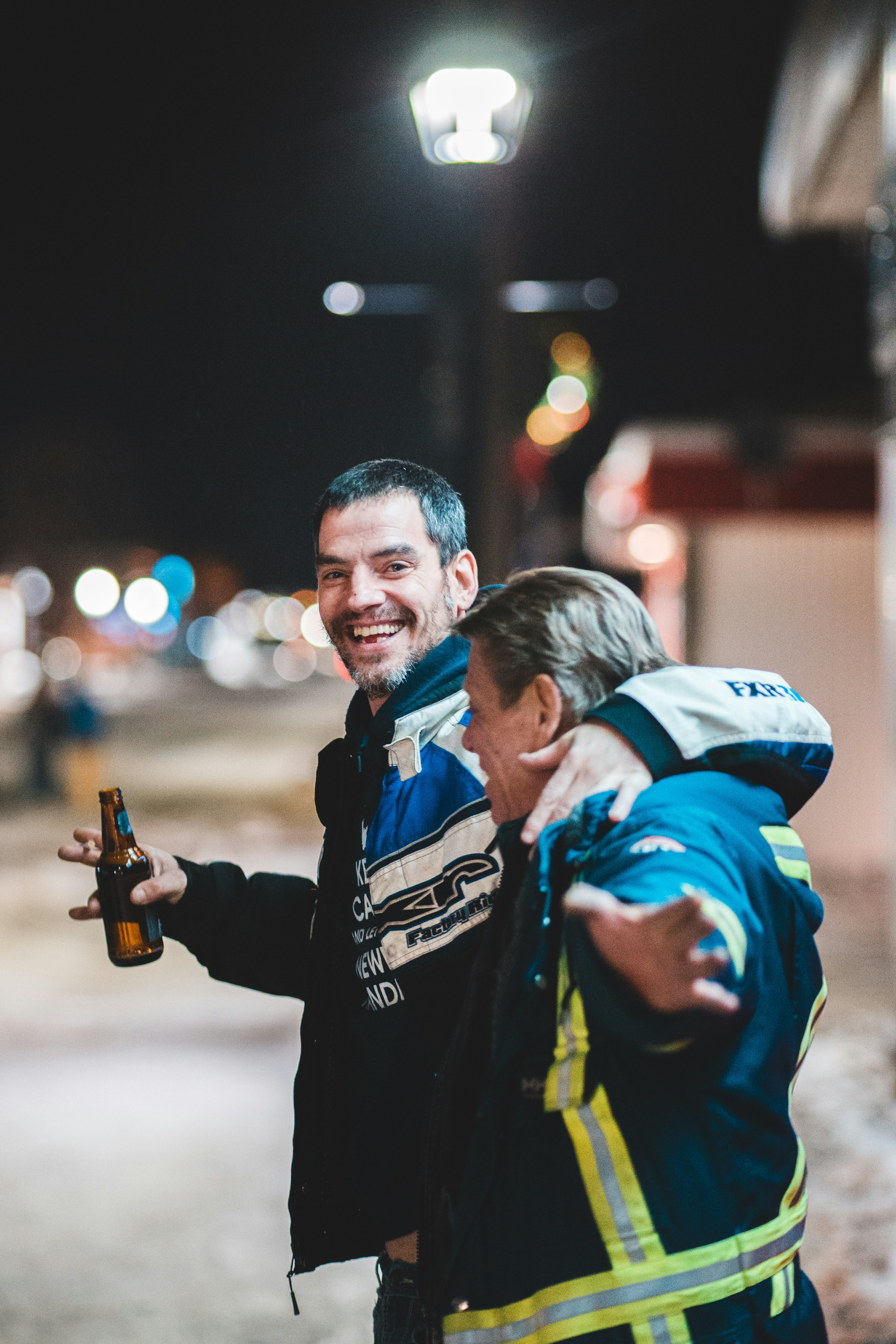 two smiling men holding holding beer bottle at night