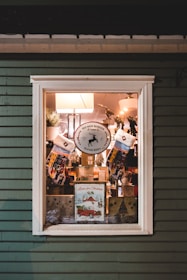 A window display showcases a festive Christmas theme with colorful stockings, a sign for Red Nose Reindeer sleigh rides, and a vintage Christmas poster featuring a red car. The scene includes lamps, greenery, and decorative elements that convey a cozy holiday atmosphere.