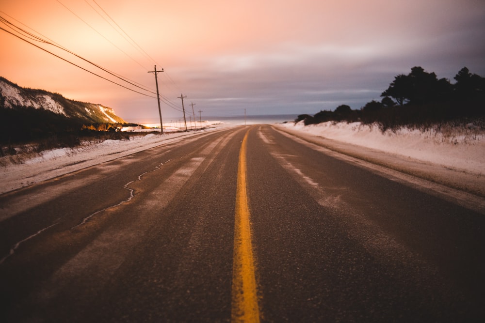 gray road near field covered with snow under white and orange sky