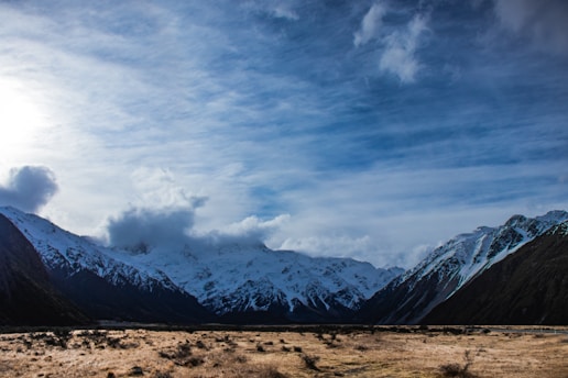A vast Patagonian landscape with snow-capped mountains and windy plains under a cloudy sky.
