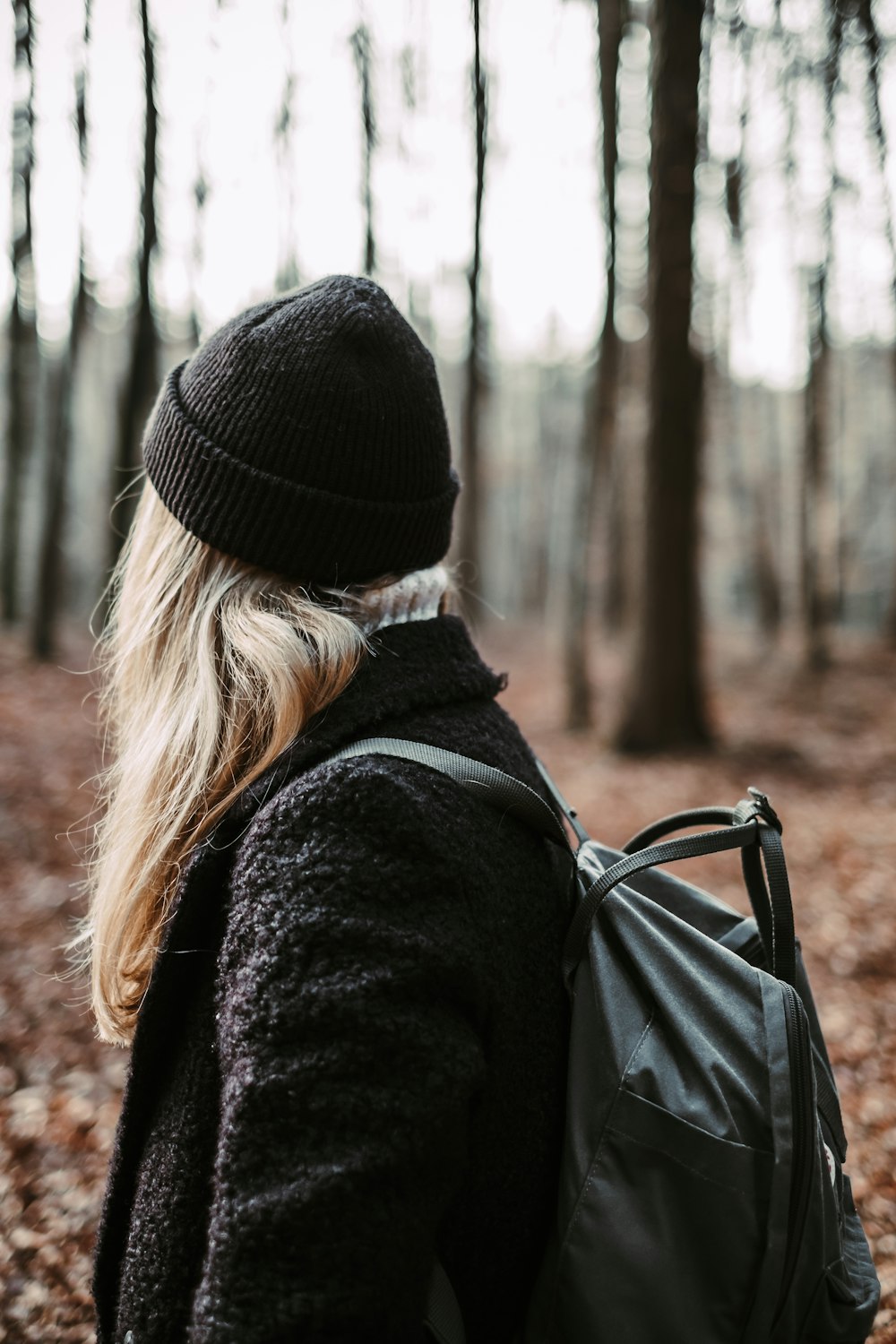 woman wearing black knit cap and jacket with backpack in forest during daytime