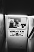 A narrow passageway leads to a small booth with a person inside wearing a hat, looking at some papers. On the booth window, there is a large sign that reads 'WANTED FULL / PART TIME DAY/NIGHT CONTROLLER' and a smaller 'WARNING' sign.