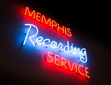 Neon lights display the words 'Memphis Recording Service' with 'Memphis' and 'Service' in red, and 'Recording' in bright blue against a dark background.