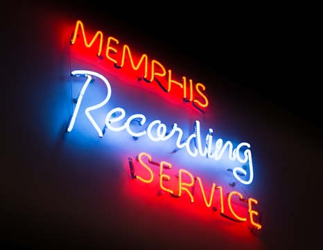 Neon lights display the words 'Memphis Recording Service' with 'Memphis' and 'Service' in red, and 'Recording' in bright blue against a dark background.
