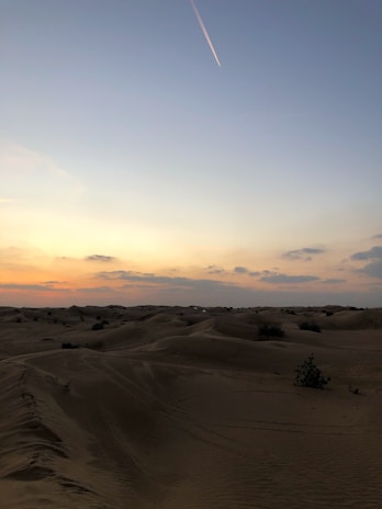 A serene desert landscape at sunset with rolling sand dunes.
