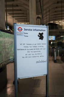 A service information board at a subway station displays a message of solidarity with Australia, expressing sorrow for the loss of life and devastation. The board includes social media handles and a shadow-like illustration of a koala.