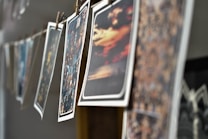 A series of photographs are hanging on a line, secured with wooden clothespins. The images feature various scenes, including landscapes and cityscapes, with vibrant colors and blurry effects. The angle of the shot provides a depth of field, focusing on the middle images while others are out of focus.