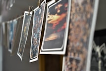 A series of photographs are hanging on a line, secured with wooden clothespins. The images feature various scenes, including landscapes and cityscapes, with vibrant colors and blurry effects. The angle of the shot provides a depth of field, focusing on the middle images while others are out of focus.