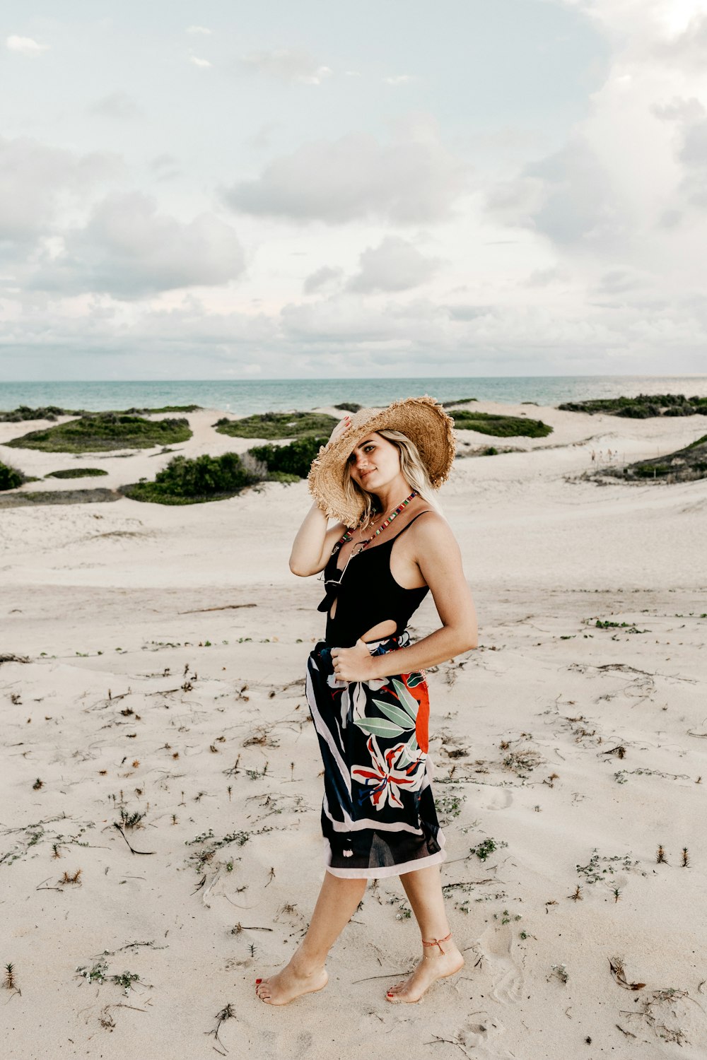 woman in black swimsuit and brown sun hat standing on shore under white sky