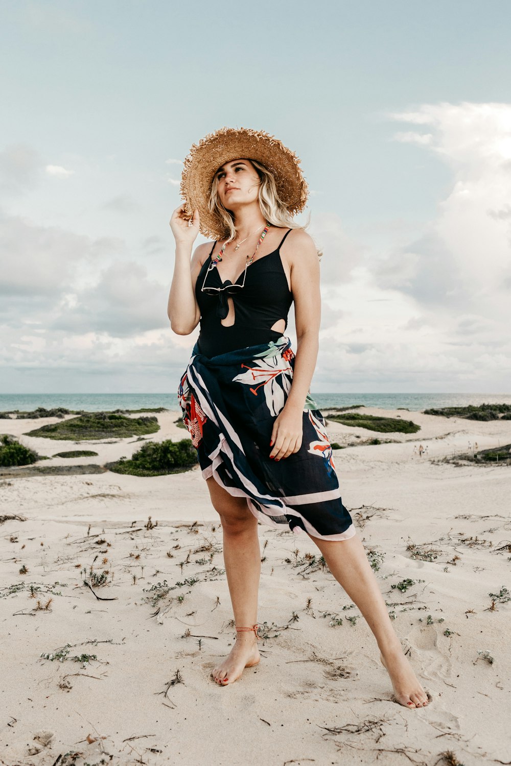 woman wearing sundress and sunhat while standing in the beach