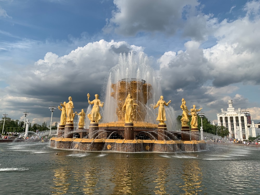 fuente de agua rodeada de estatuas bajo el cielo nublado azul
