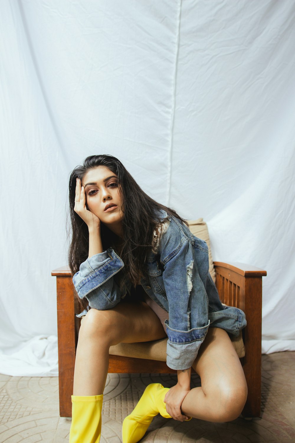 woman in blue denim jacket and yellow boots sitting on wooden armchair