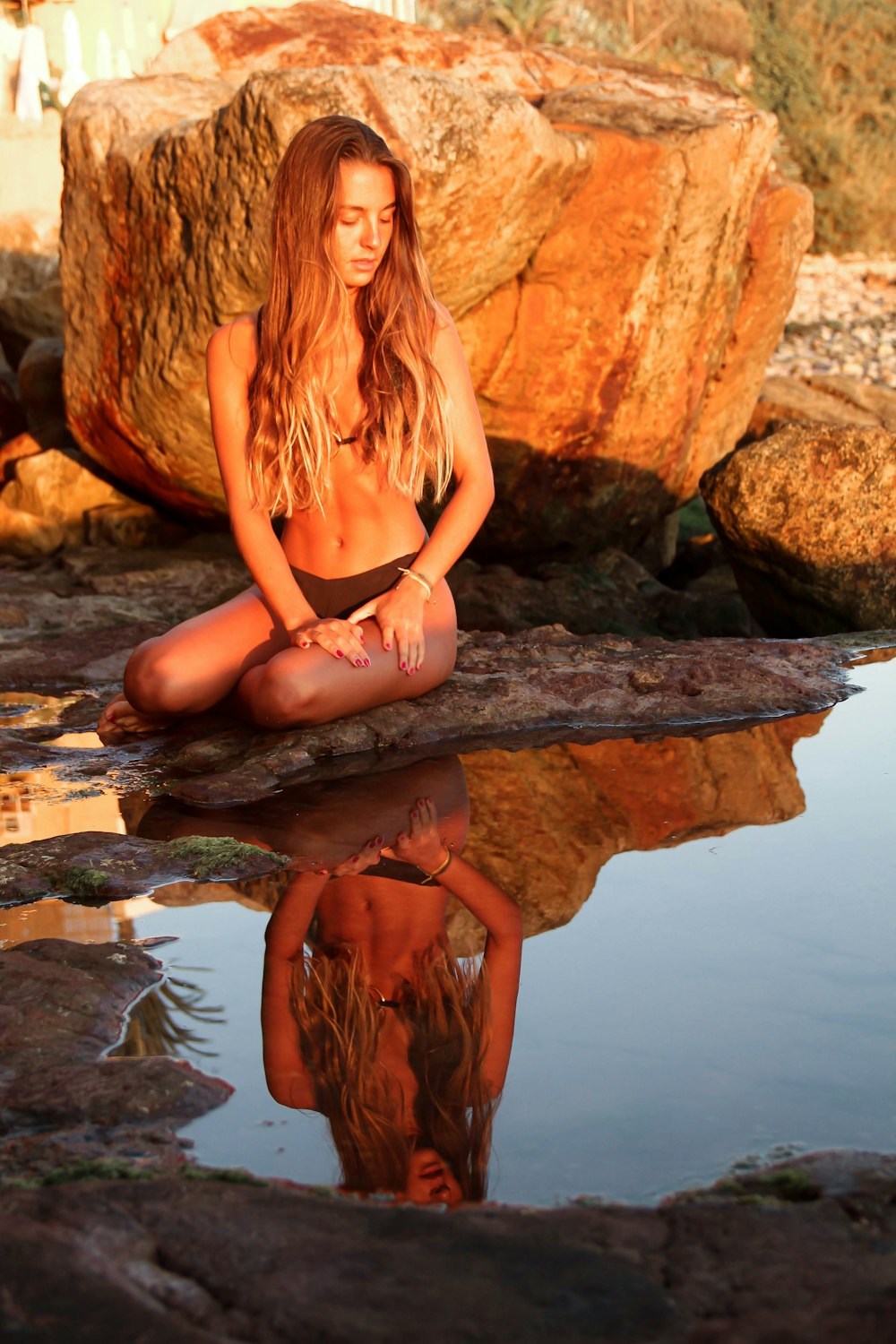 woman wearing grey bikini sitting near the brown stone
