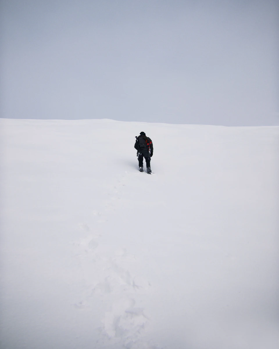Lone hiker in black clothing ascends steep hill with visible footprints in snowy landscape
