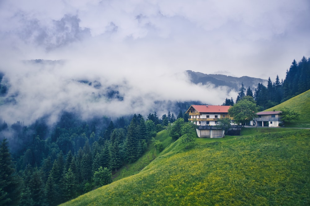 landscape photography of white and red 3-storey house beside green mountain ranges under white fogs during daytime