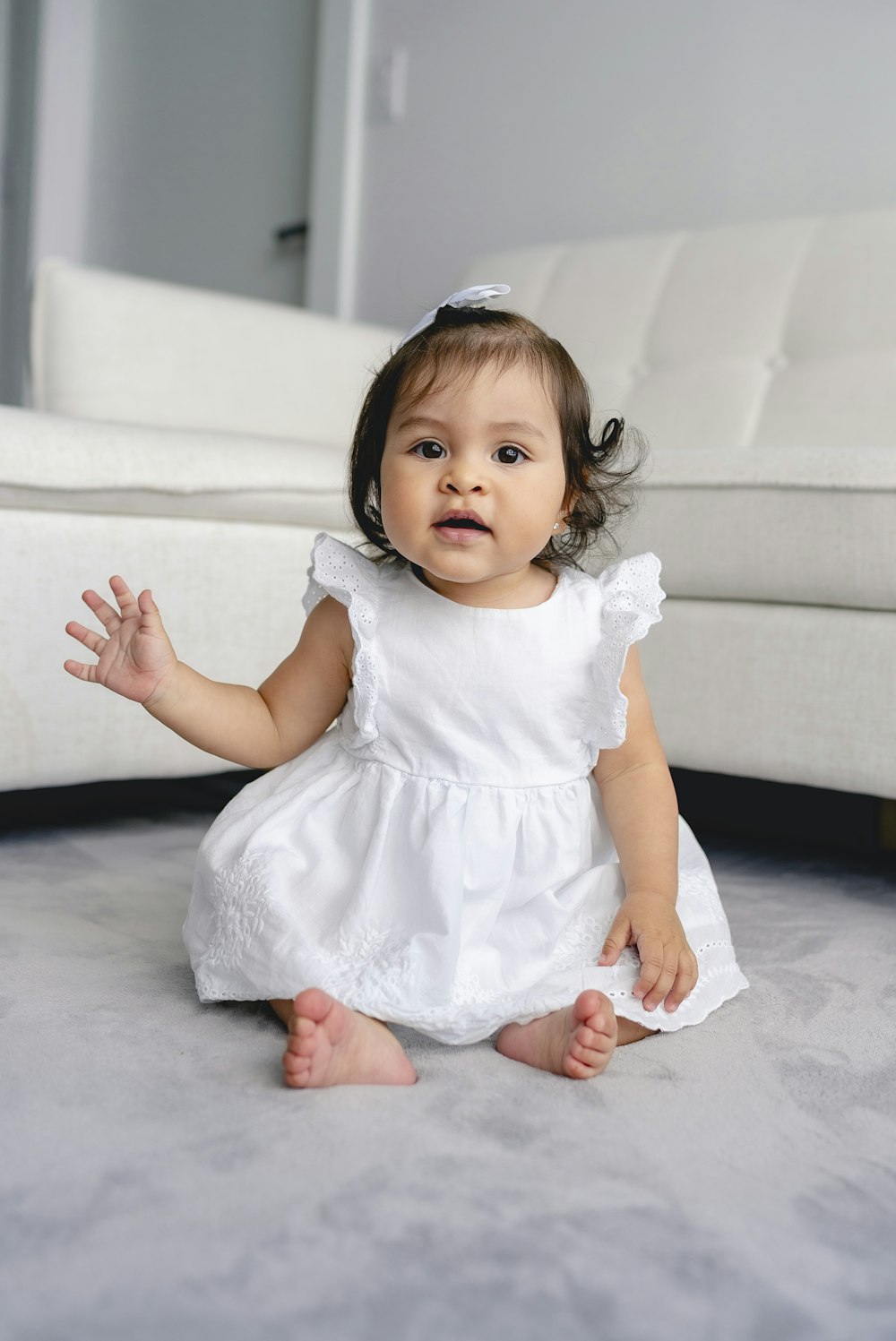 toddler wearing white dress sitting beside white sofa