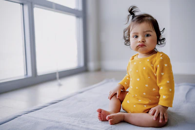 Toddler wearing a soft yellow onesie with a playful design, sitting by a window filled with natural light.