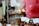 A display of assorted baked goods, featuring cupcakes with sprinkles on a wooden stand, surrounded by various cookies and pastries with price tags. Some of the tags identify items like flourless chocolate pecan sandwich cookies and whoopie pies. A blurred figure is visible in the background.