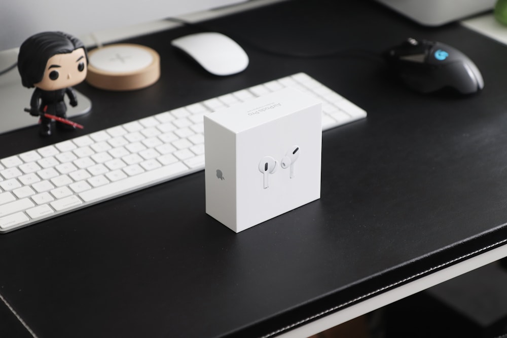 책상 위의 Apple Magic 키보드 옆에 흰색 이어버드 상자