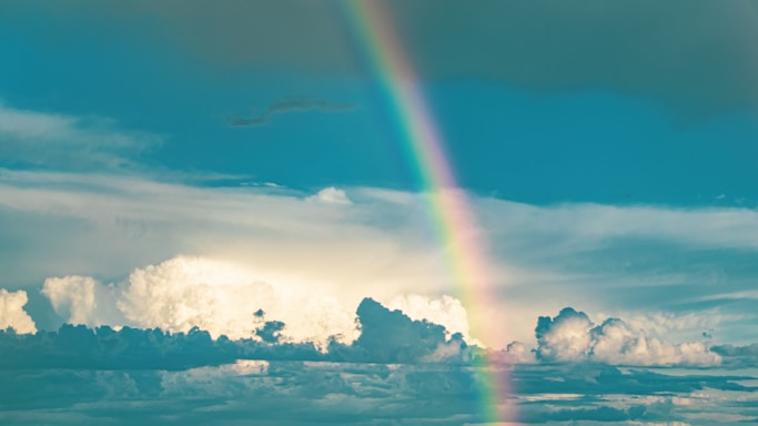 Sunshine spilling over a vibrant rainbow with cheerful clouds above.