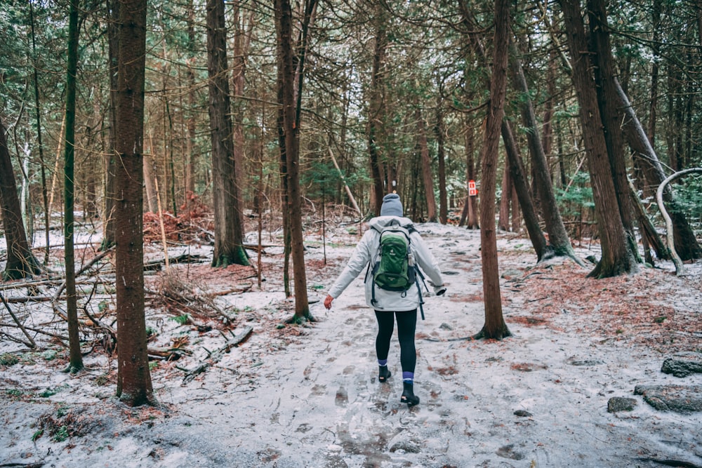 woman wearing white jacket carrying backpack standing beside trees