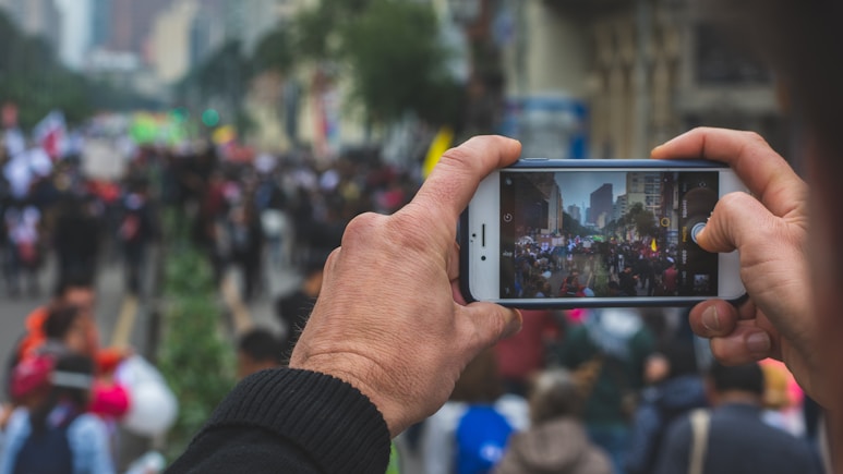 selective focus photography of person taking photo of crowd during daytime
