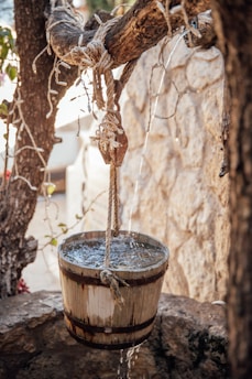 A sturdy blue plastic water bucket filled with fresh water, sitting on a wooden dock by the river.