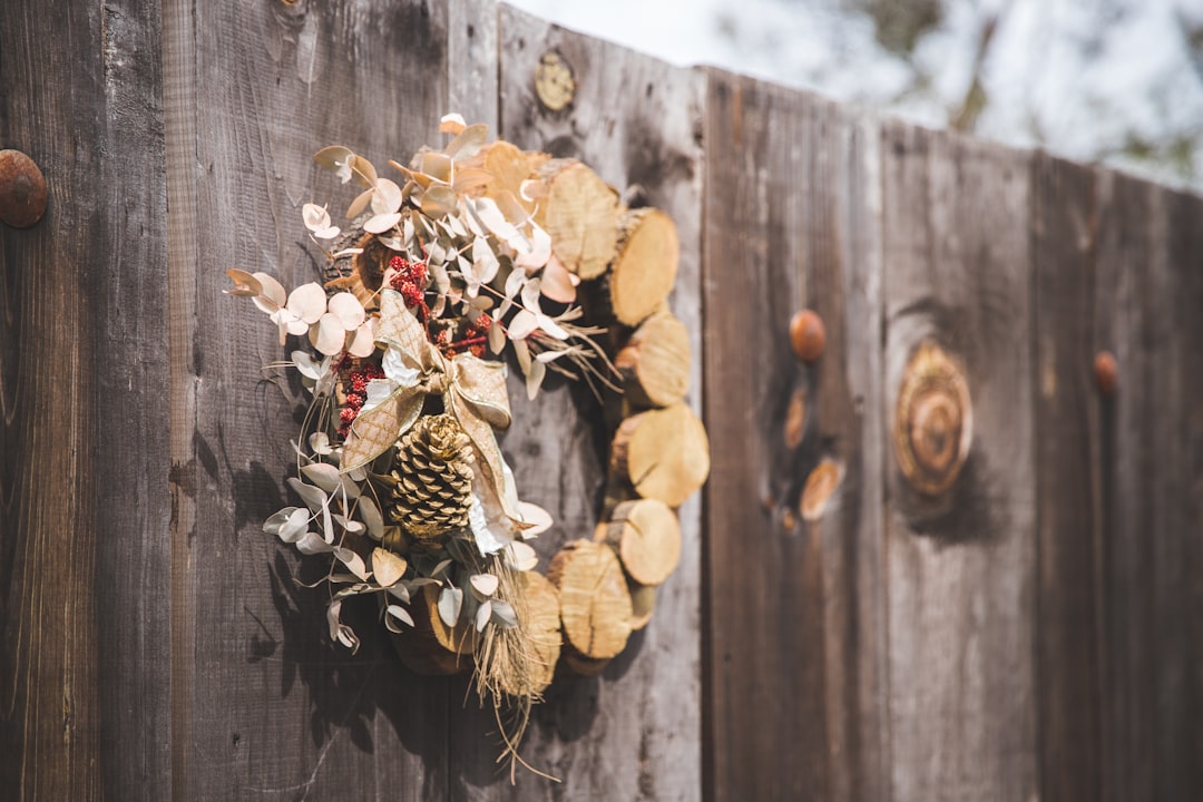 brown wreath with pine cone hanging on wooden fence