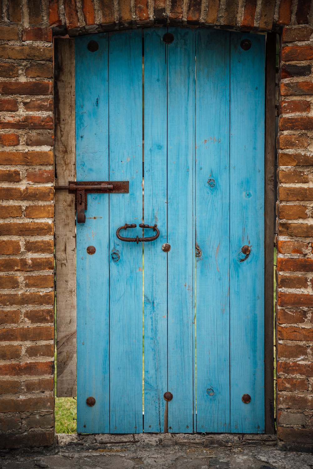 Puerta de tablones de madera azul y pared de ladrillo