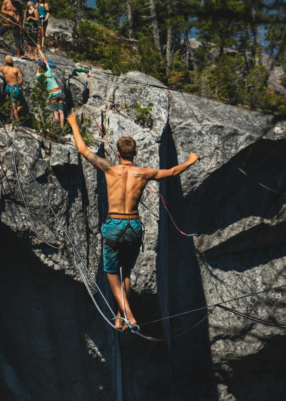 uomo in topless che indossa pantaloncini blu che calpesta la corda tra la montagna