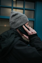 man in gray beanie hat and black jacket using smartphone