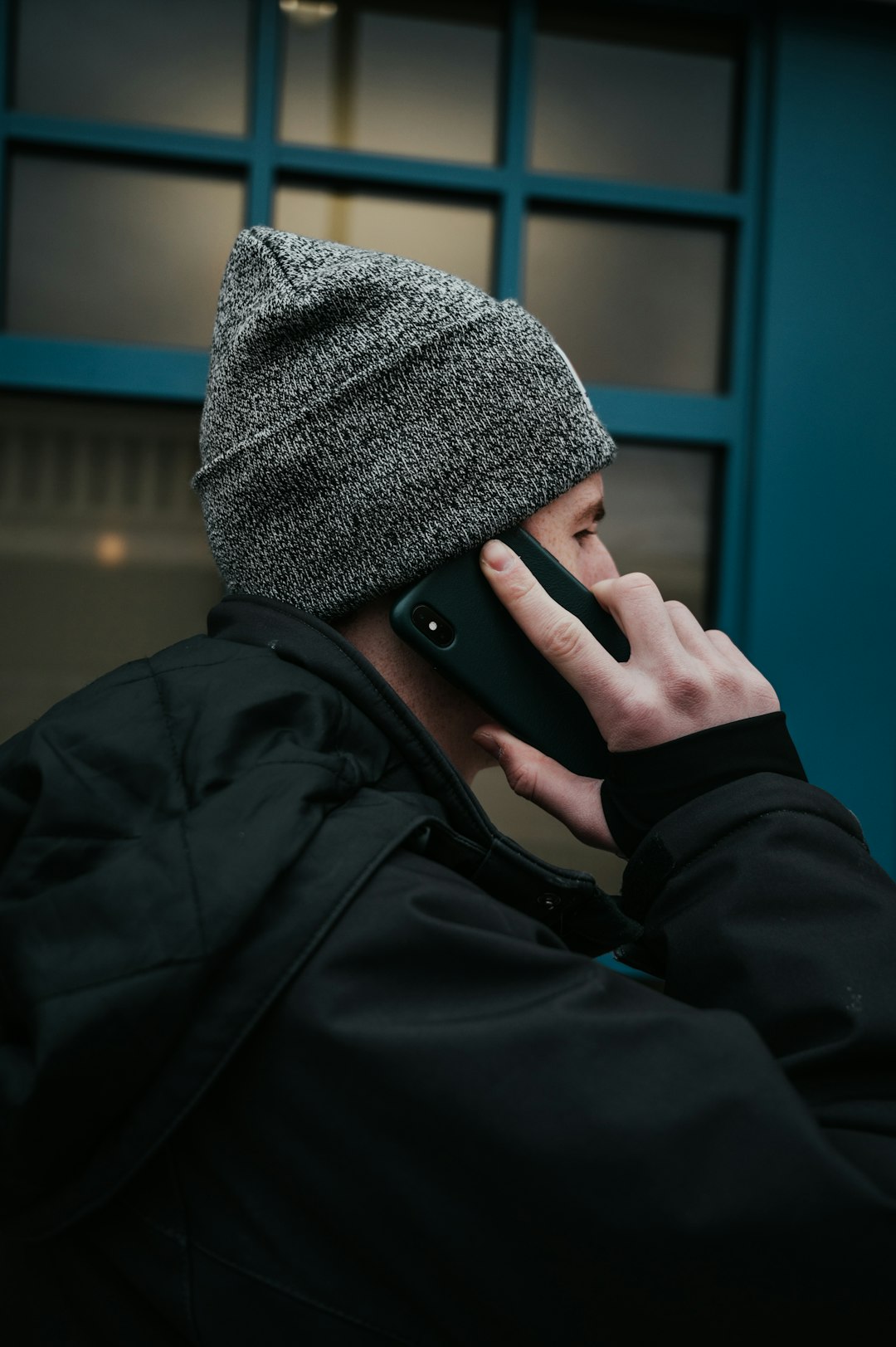 man in gray beanie hat and black jacket using smartphone