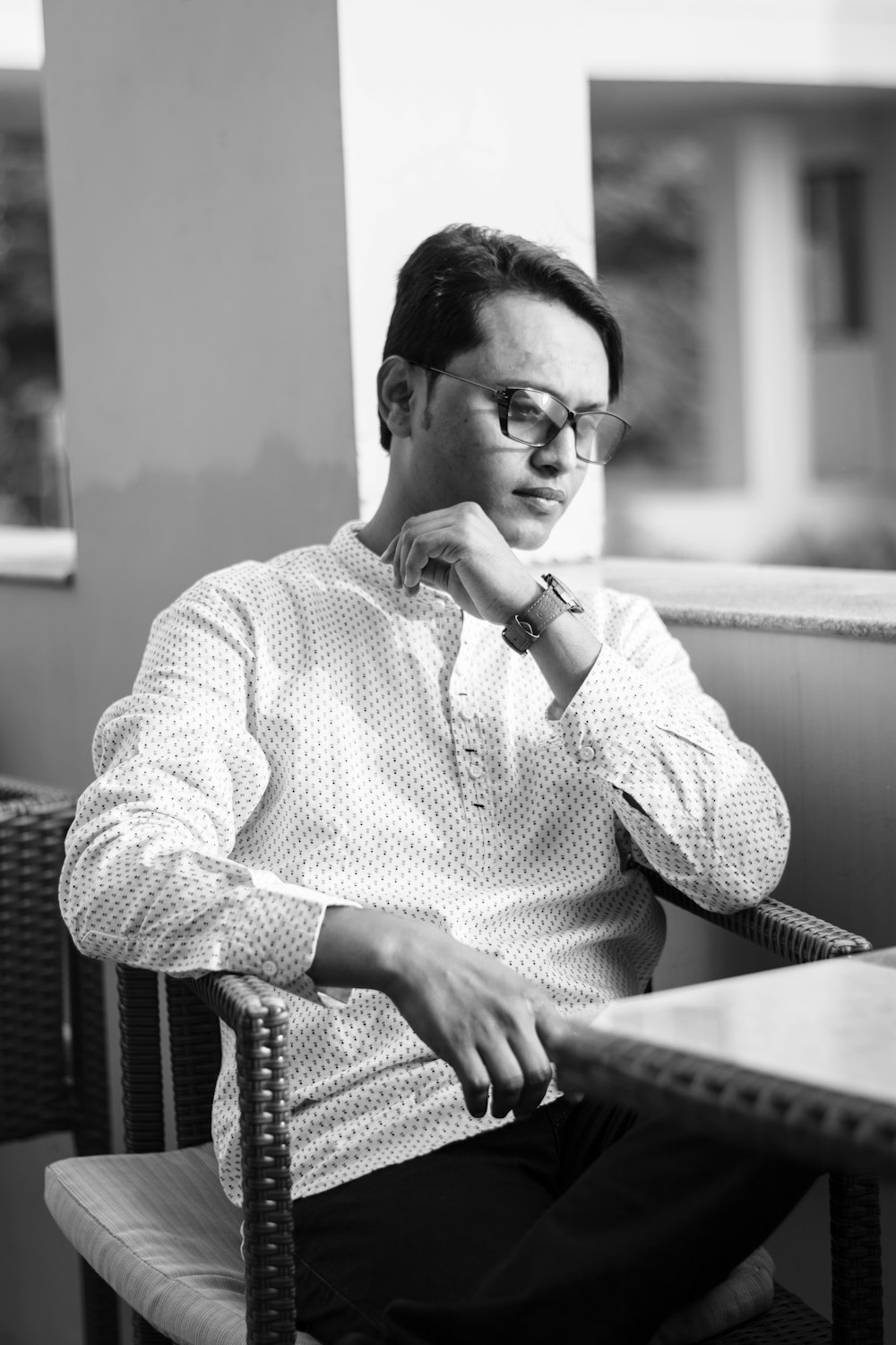 grayscale photography of man wearing long-sleeved shirt sitting with crossed legs near table