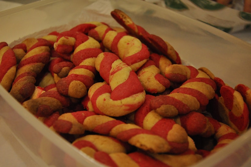 A collection of twisted cookies with alternating red and yellow colors is placed in a translucent plastic container.