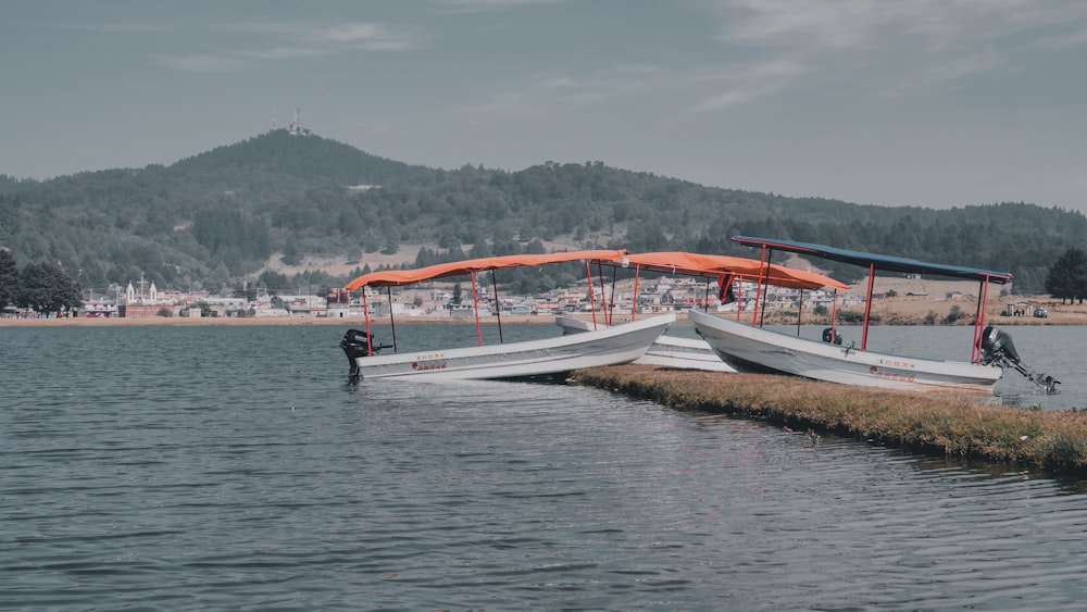 white and orange boats near body of water viewing mountain under blue and white sky