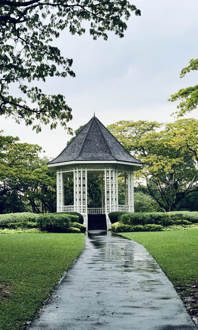 The white lattice Bandstand gazebo at Singapore Botanic Gardens at the end of a path, framed by lawn and trees.