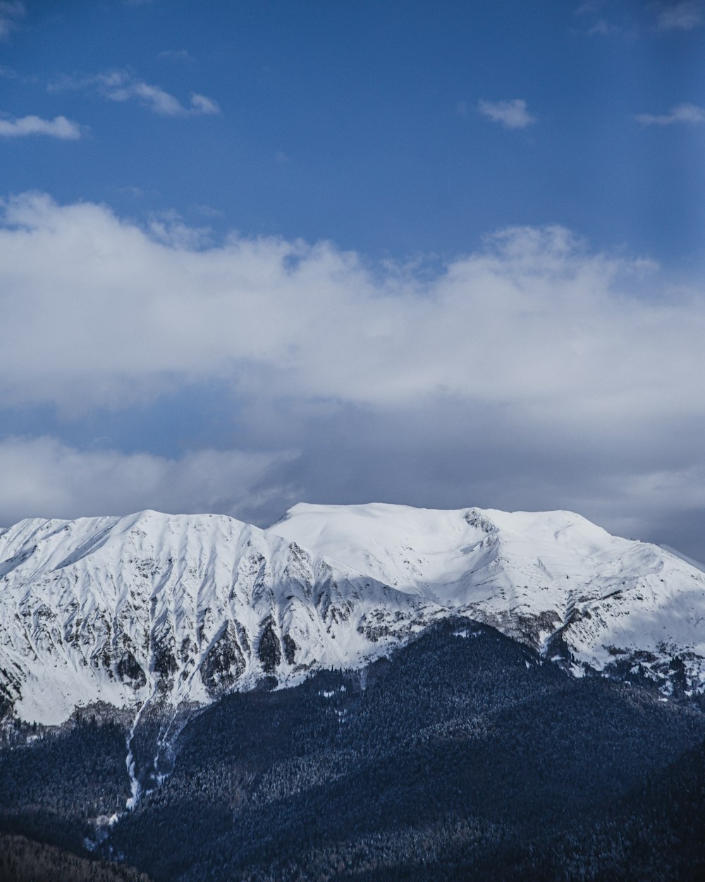 Fotografía aérea de la cumbre de la montaña cubierta de nieve bajo el cielo blanco y azul