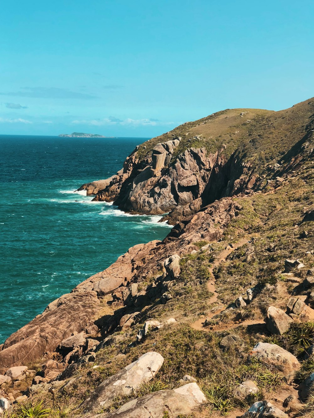 aerial photography of beach cliff viewing blue sea under blue and white sky