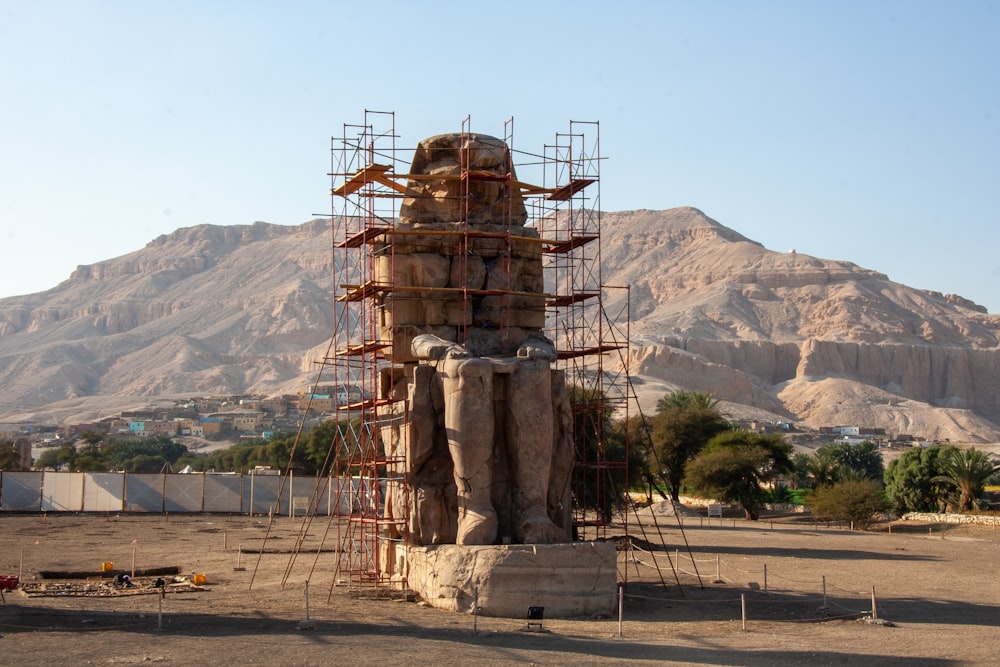 sitting Egyptian statue on soil field near trees during day