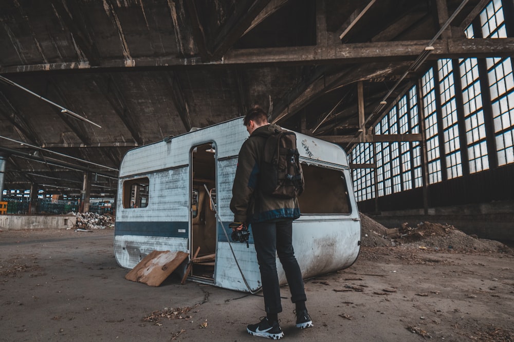 man standing beside abandoned camper trailer inside building