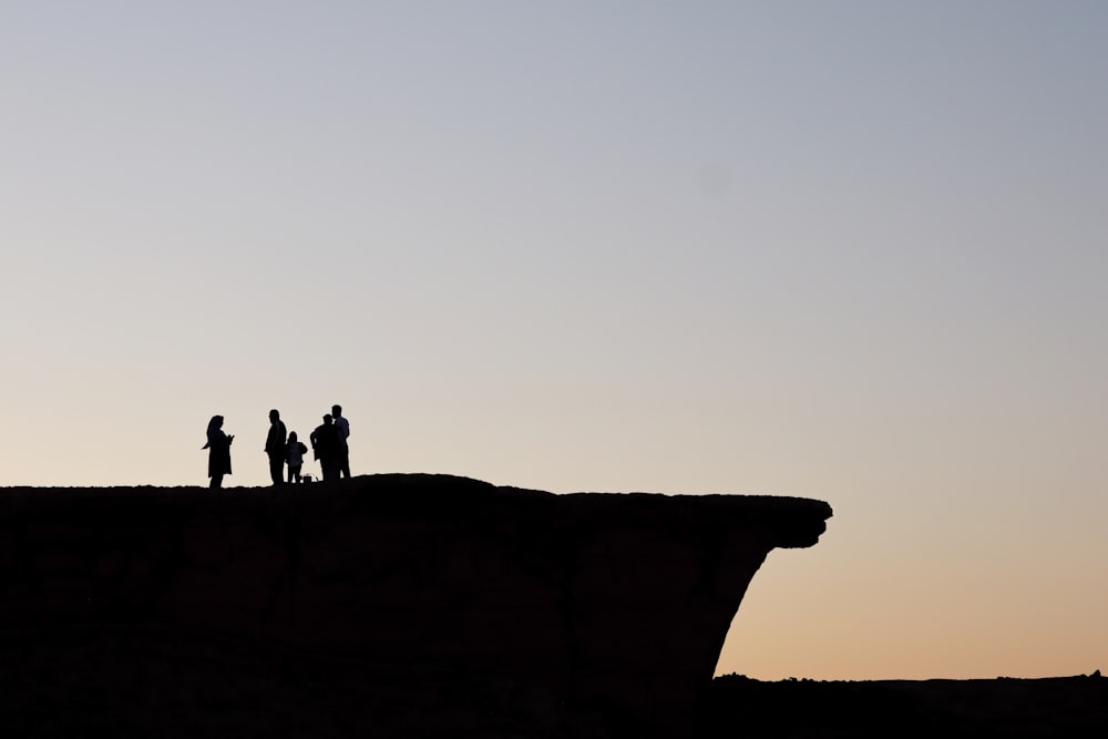 silhouette of people standing on cliff