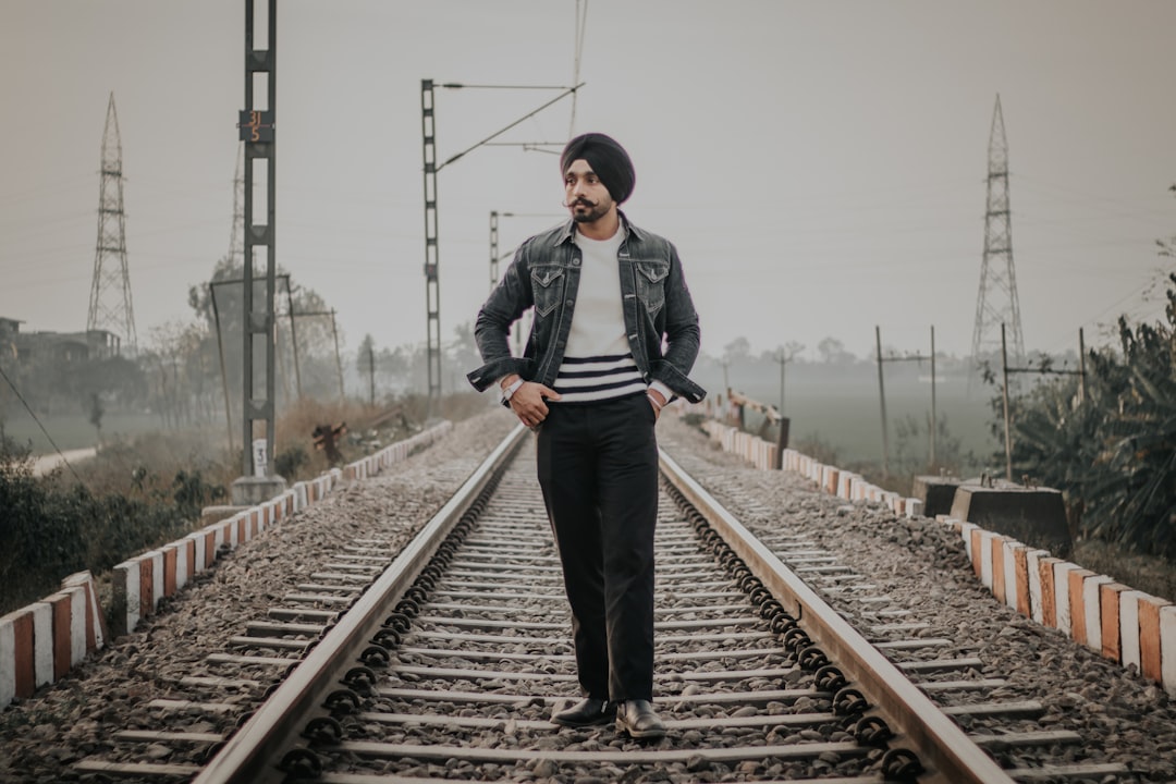 man wearing blue jacket and black turban hat standing on train railway during daytime